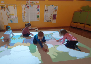 Czworo dzieci bawi się na podłodze interaktywnej. Dzieci rozganiają chmurki.